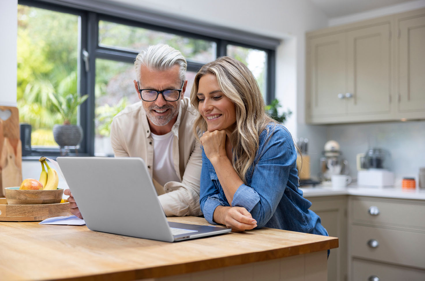 A couple in their modern kitchen looking at their laptop on the kitchen counter and smiling