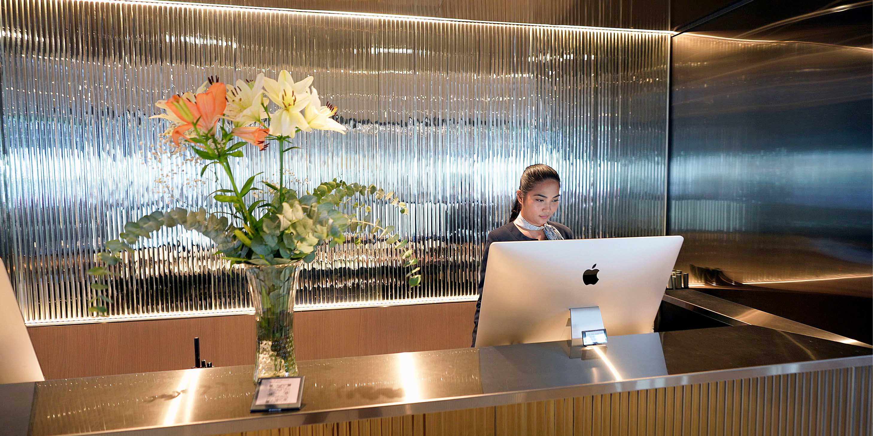 flowers in a vase on top of the reception desk with a staff member standing behind a computer screen working
