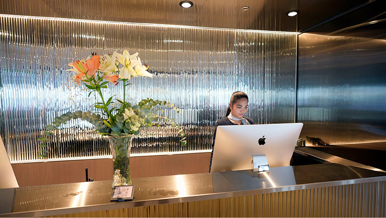 flowers in a vase on top of the reception desk with a staff member standing behind a computer screen working