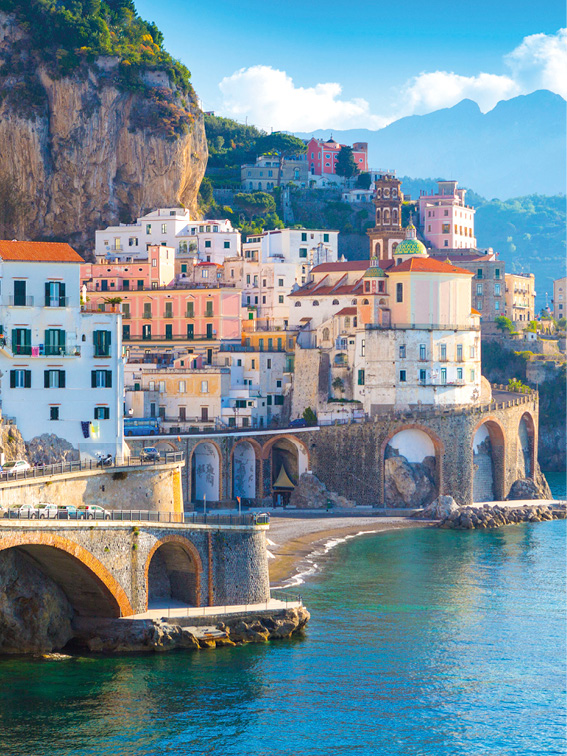 Buildings on the Amalfi Coast cliff face, with blue water to the right and hills behind