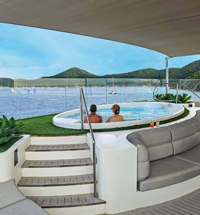 Guests relaxing in a spa pool on a yacht with ocean and hills in the background