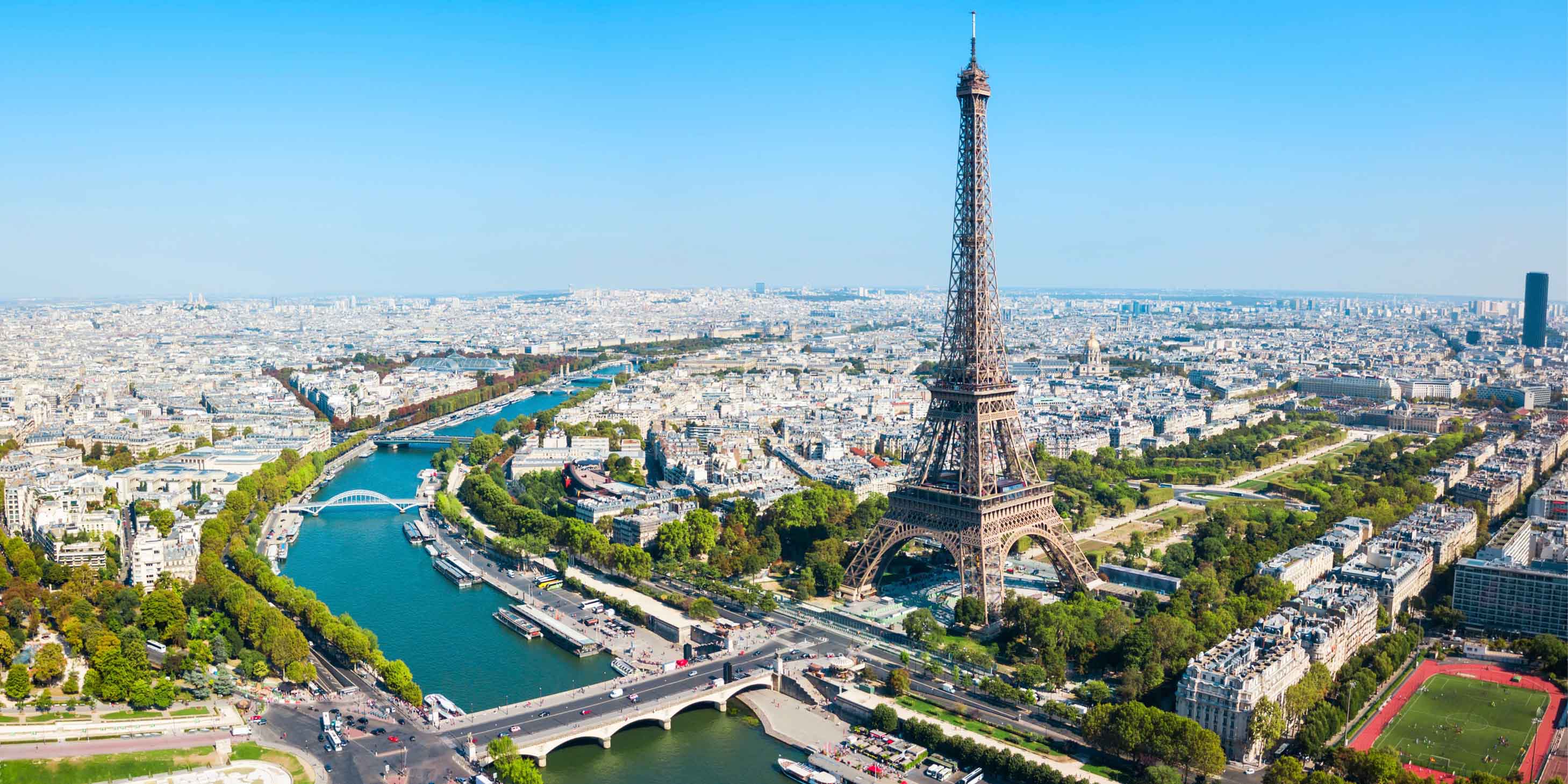 Aerial view of Paris, with the Eiffel Tower and River Seine in clear view, a blue sky above
