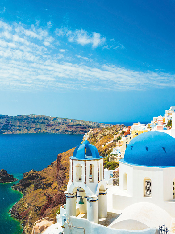 Blue-domed church of Santorini, Greece on a bright sunny day, with light cloudy sky and deep blue sea
