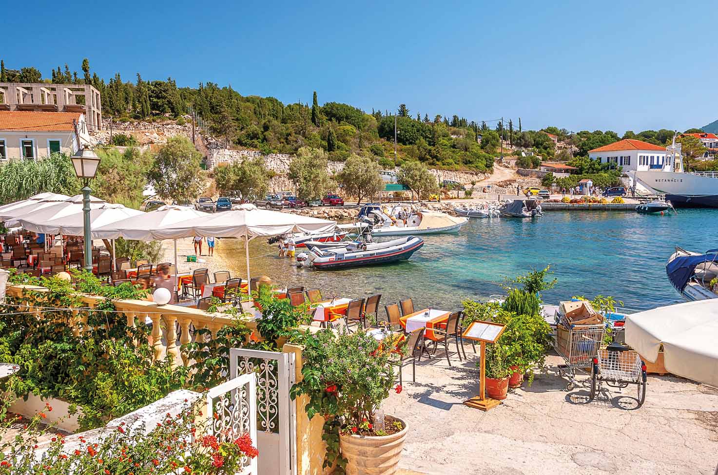 Traditional seafront restaurant with wooden tables, white tablecloths and white umbrellas looking over the bay in Fiskardo, Cephalonia 