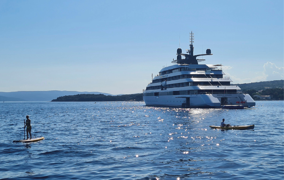 A luxury yacht on the dazzling blue sea near the coast, with a kayaker in the foreground enjoying the blue skies. 