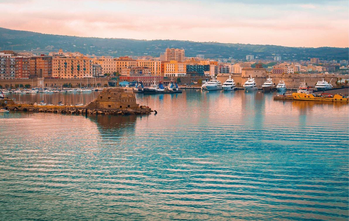 Port Civitavecchia, Italy, as sun sets giving the buildings a golden glow, with ripples forming on the crystal blue waters