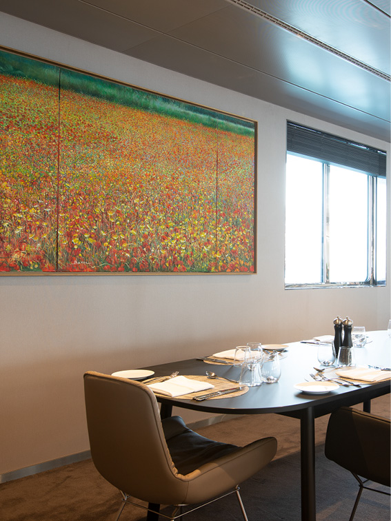 Les Coquelicots, a painting of wild poppies, situated on a dining room wall next to the windows in front of a set dining table