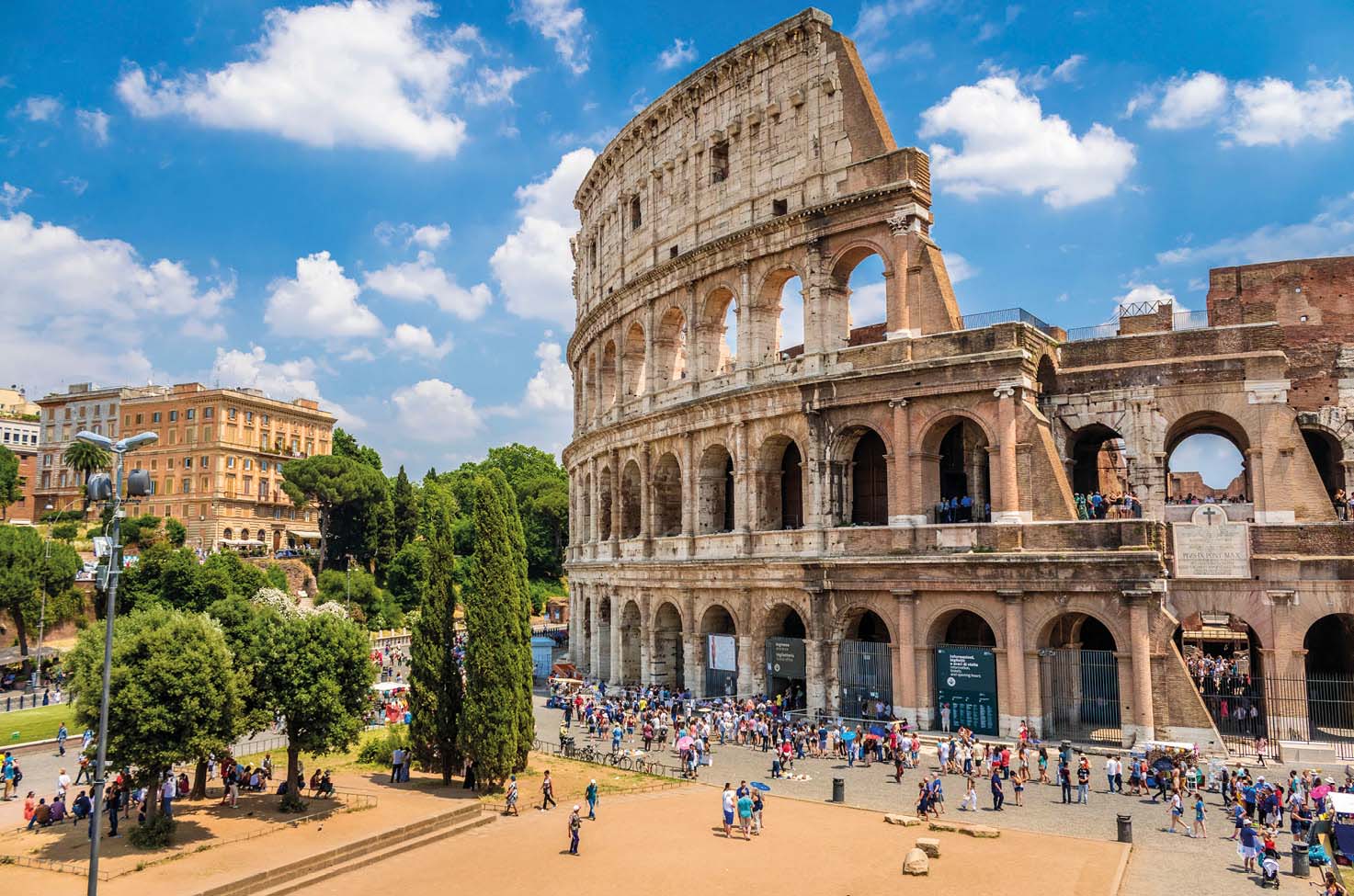 Panorama view of the Colosseum in Rome, with a blue sky and clouds, and tourists walking by