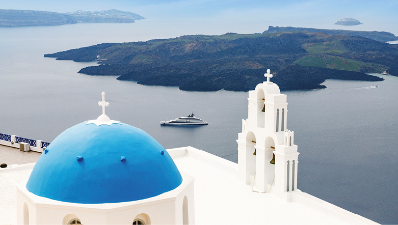 Luxury yacht sailing near the coast of Santorini surrounded by the iconic whitewashed buildings with blue rooftops