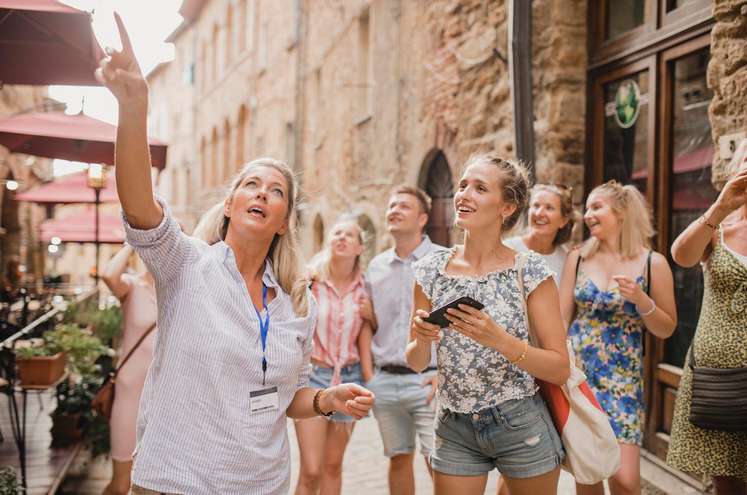 City tour guide pointing up, as her audience of six smiles, listens, and looks in the direction she is pointing