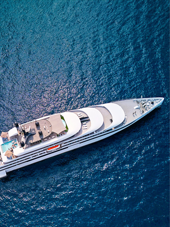A luxury yacht floats on a dark blue ocean, seen from a bird’s-eye view 