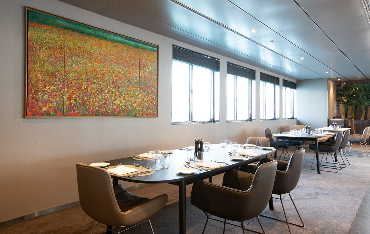 A painting of a field of red and yellow flowers hangs on the wall of an airy and stylish restaurant