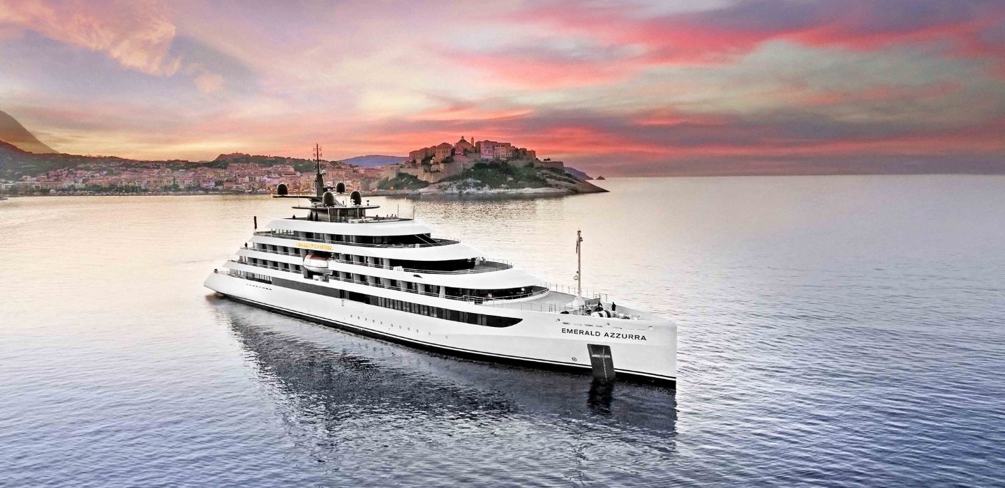 An Emerald Cruises luxury yacht cruise anchored in Calvi, Corsica, France, set against a dramatic red sky at sunset